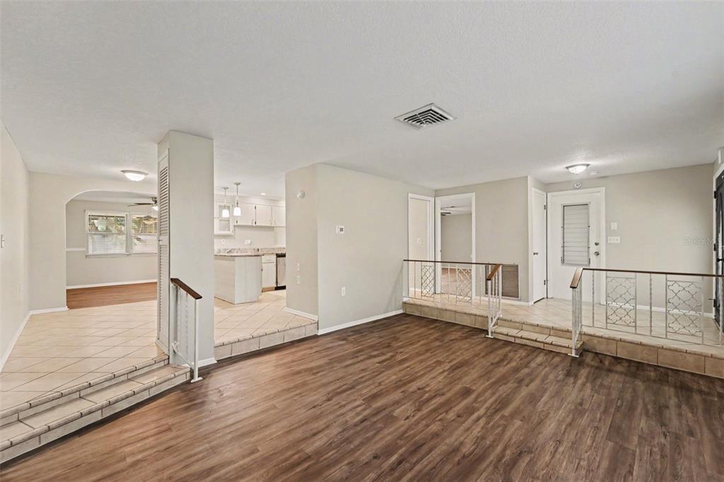 A sunken living room with wood-look flooring transitions to tiled areas with decorative metal railings — 5751 DOLORES DRIVE, HOLIDAY, FL