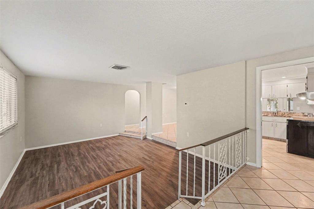 A split-level room features wood-look flooring, a white metal railing, and a tiled kitchen entrance — 5751 DOLORES DRIVE, HOLIDAY, FL