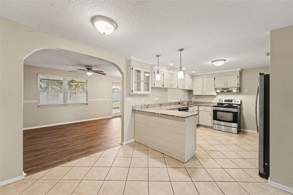 A kitchen with light cabinets and granite countertops opens into a dining area with flooring — 5751 DOLORES DRIVE, HOLIDAY, FL