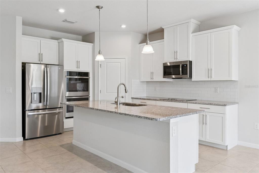 A modern kitchen features white cabinets, stainless steel appliances, and a granite-topped island — 2106 HAVASU FALLS DRIVE, DELAND, FL