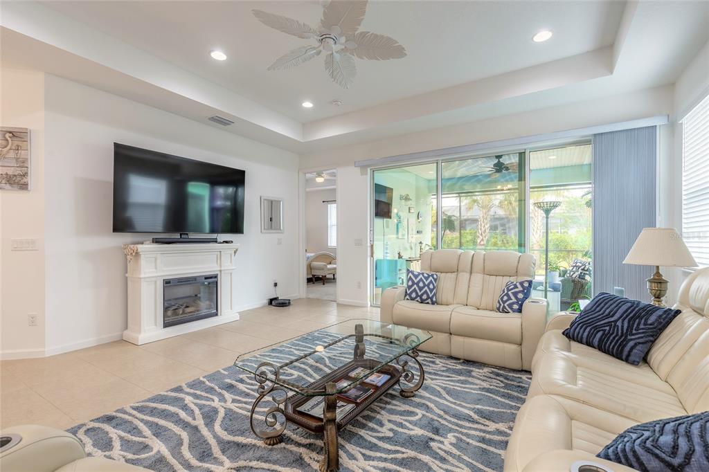 A living room with a fireplace, television, white leather sofas, and a large glass sliding door — 230 SAND BAR LANE, DAYTONA BEACH, FL