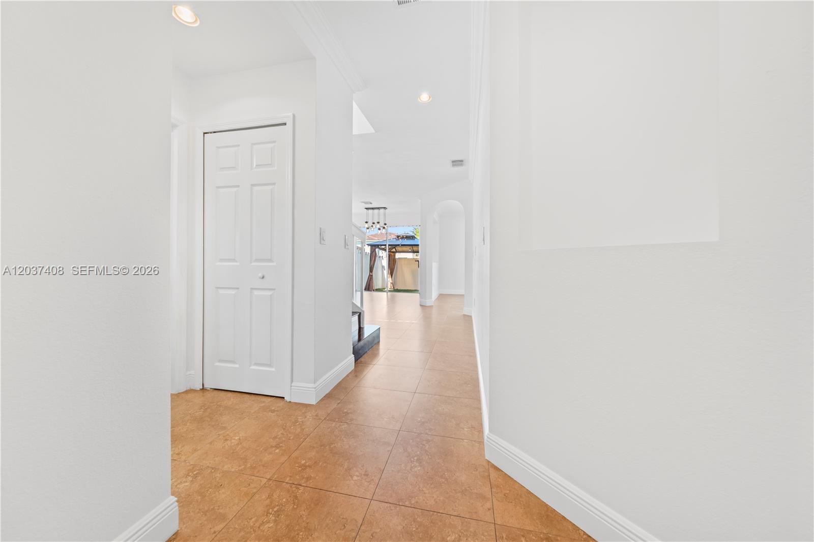 A hallway with white walls and tiled floors leads toward a view of a patio — 27460 SW 138th Path, Homestead FL 33032, HOMESTEAD, FL