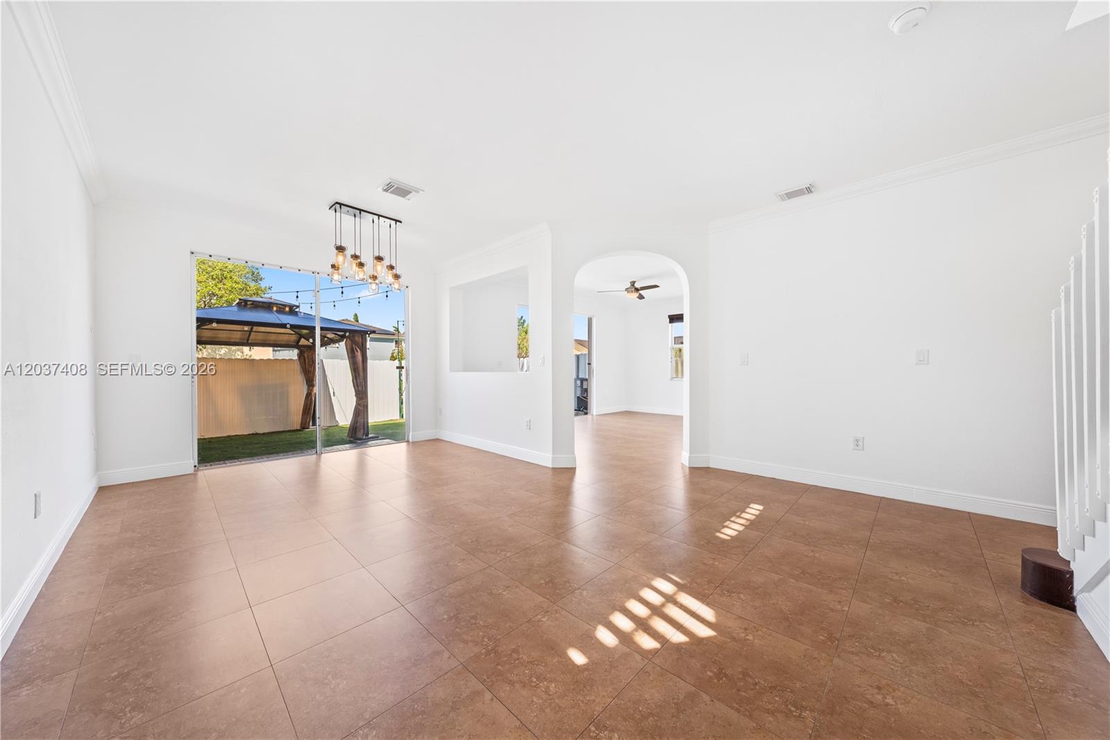 An empty room with brown tile floors, a chandelier, and a sliding glass door — 27460 SW 138th Path, Homestead FL 33032, HOMESTEAD, FL