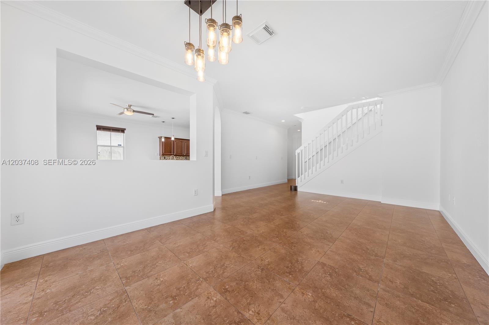 An open dining area features brown tile flooring, a modern chandelier, and a staircase — 27460 SW 138th Path, Homestead FL 33032, HOMESTEAD, FL