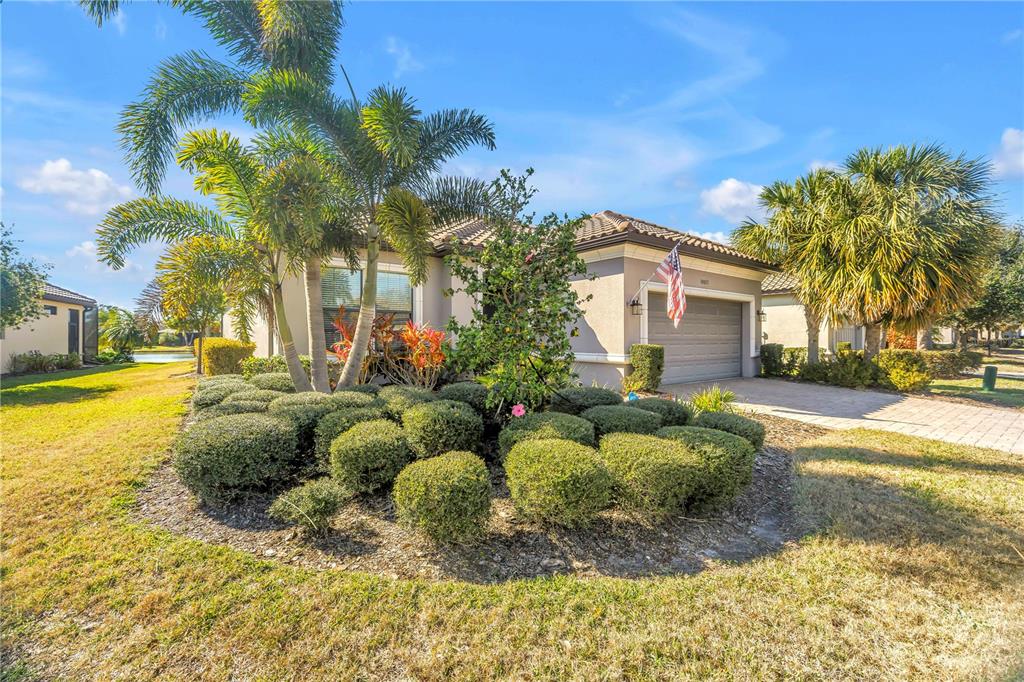 A single-story house with a paved driveway, palm trees, and a manicured shrub garden — 10025 CRAFTSMAN PARK WAY, PALMETTO, FL