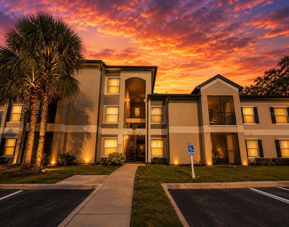 A multi-story apartment building exterior at sunset with a palm tree and a parking lot — 8939 LATREC AVENUE UNIT 1303, ORLANDO, FL