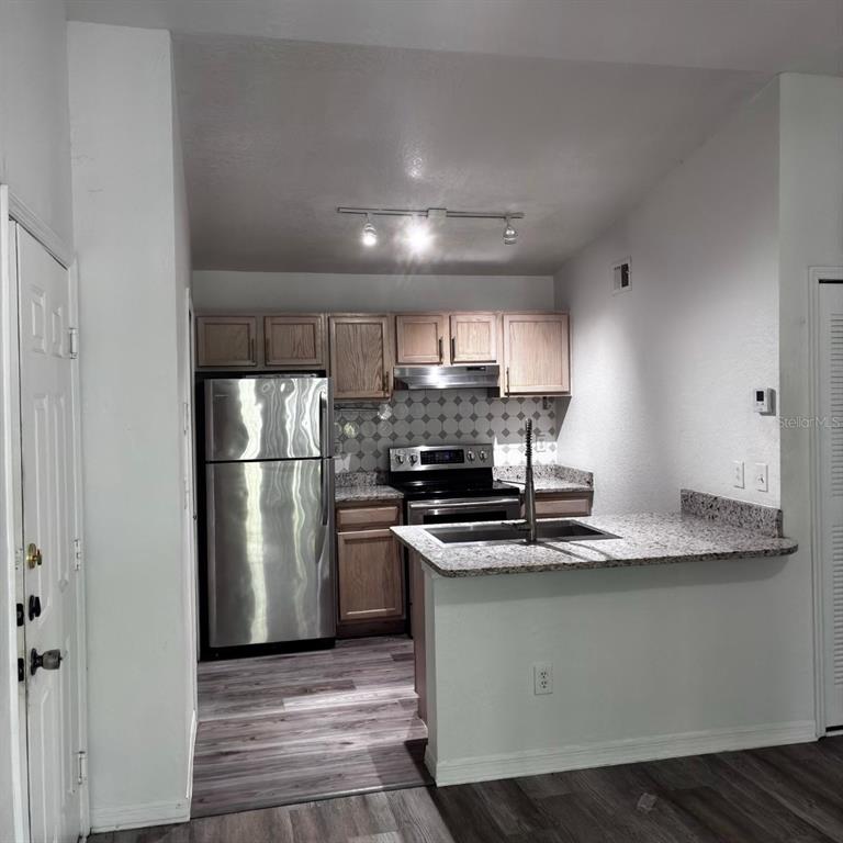 A kitchen features wood cabinets, stainless steel appliances, granite countertops, and wood-look flooring — 8939 LATREC AVENUE UNIT 1303, ORLANDO, FL