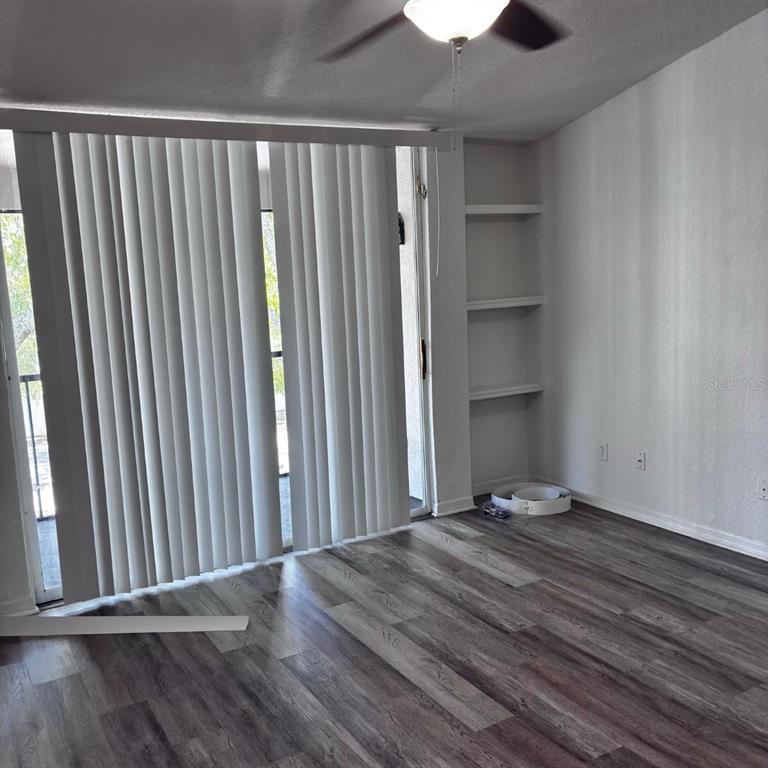 A room with wood-look flooring, vertical blinds on a sliding door, and built-in wall shelves — 8939 LATREC AVENUE UNIT 1303, ORLANDO, FL
