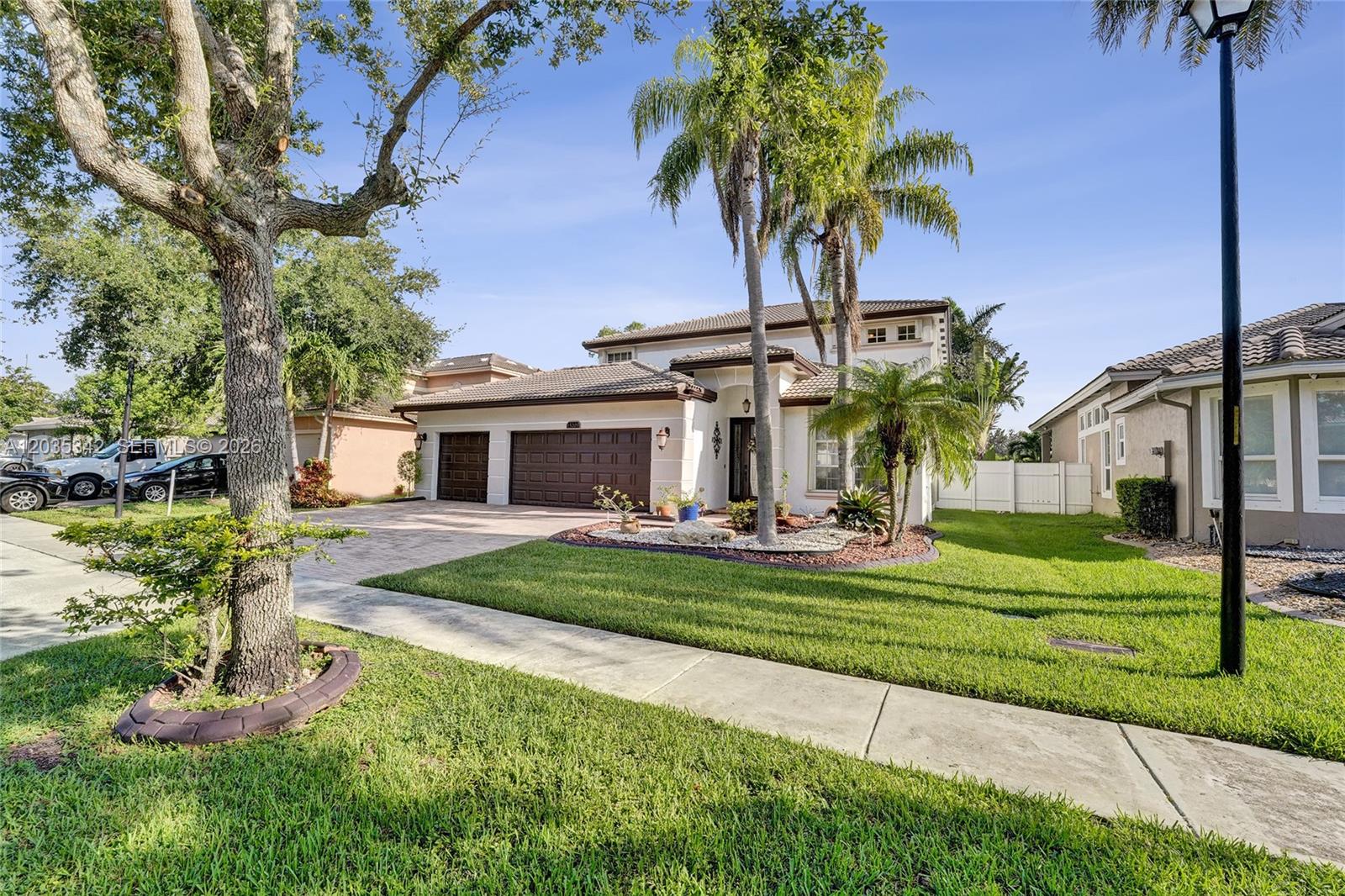 A two-story suburban house features a paved driveway, a three-car garage, and palm trees — MIRAMAR, FL