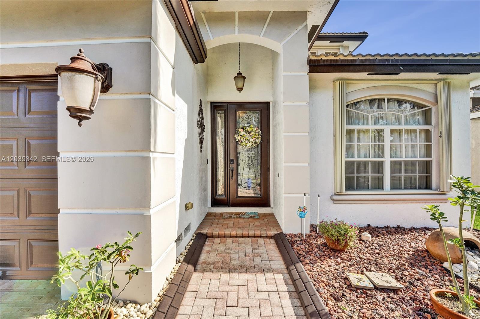 The exterior of a house features a brick walkway leading to a dark wood front door — MIRAMAR, FL