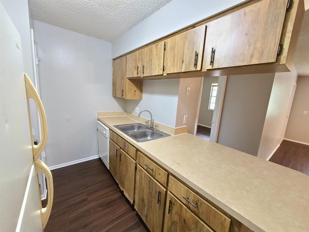 A kitchen features wood cabinets, laminate countertops, a double sink, and dark wood-look flooring — 205 RED MAPLE PLACE UNIT 205, BRANDON, FL