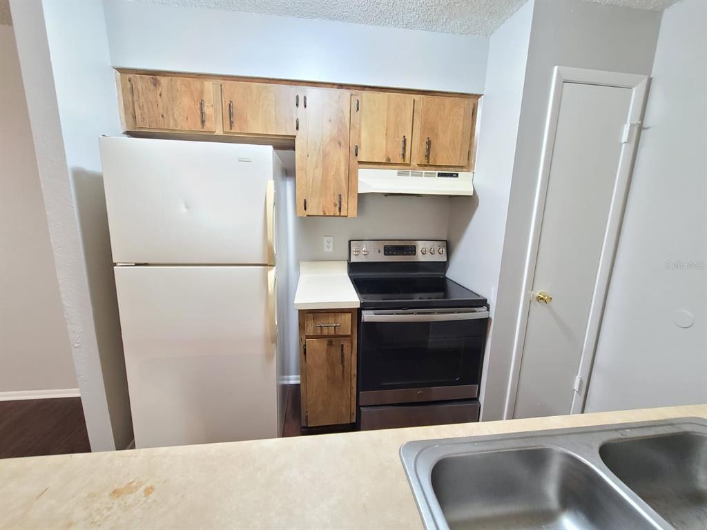A kitchen features wood cabinets, a white refrigerator, a black electric stove, and a sink — 205 RED MAPLE PLACE UNIT 205, BRANDON, FL