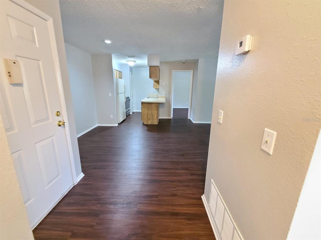 An interior view shows a living area with dark wood flooring leading to a kitchen — 205 RED MAPLE PLACE UNIT 205, BRANDON, FL