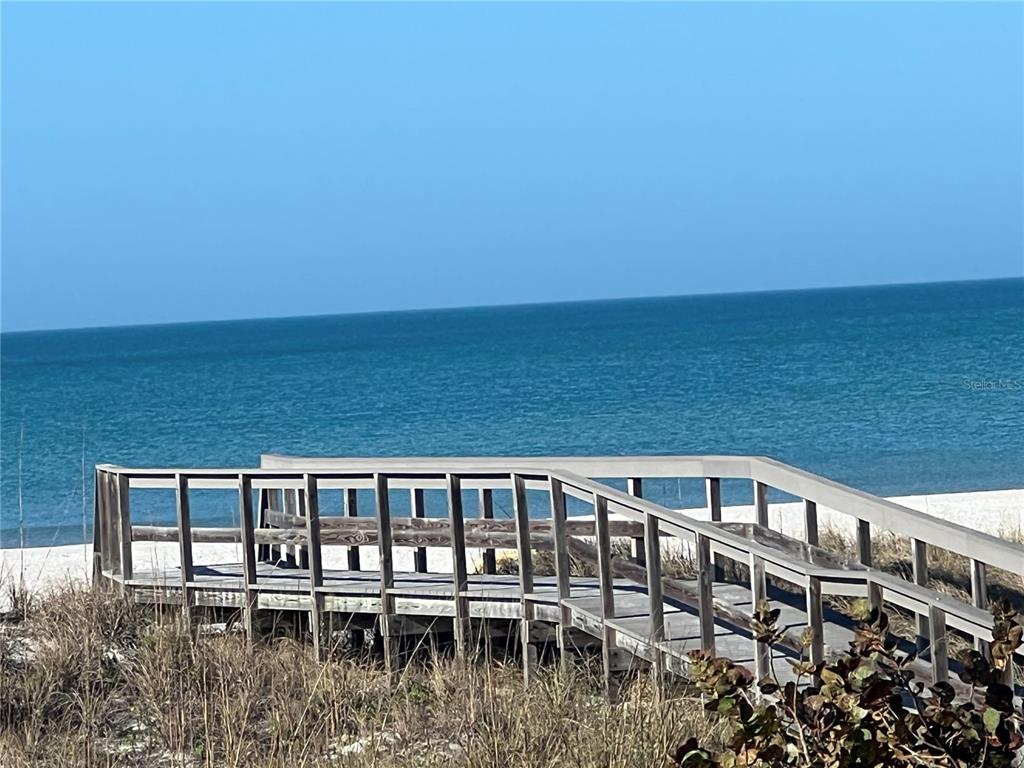 A wooden boardwalk leads through sand dunes toward the ocean under a clear blue sky — 200 120TH AVENUE W UNIT 3A, TREASURE ISLAND, FL
