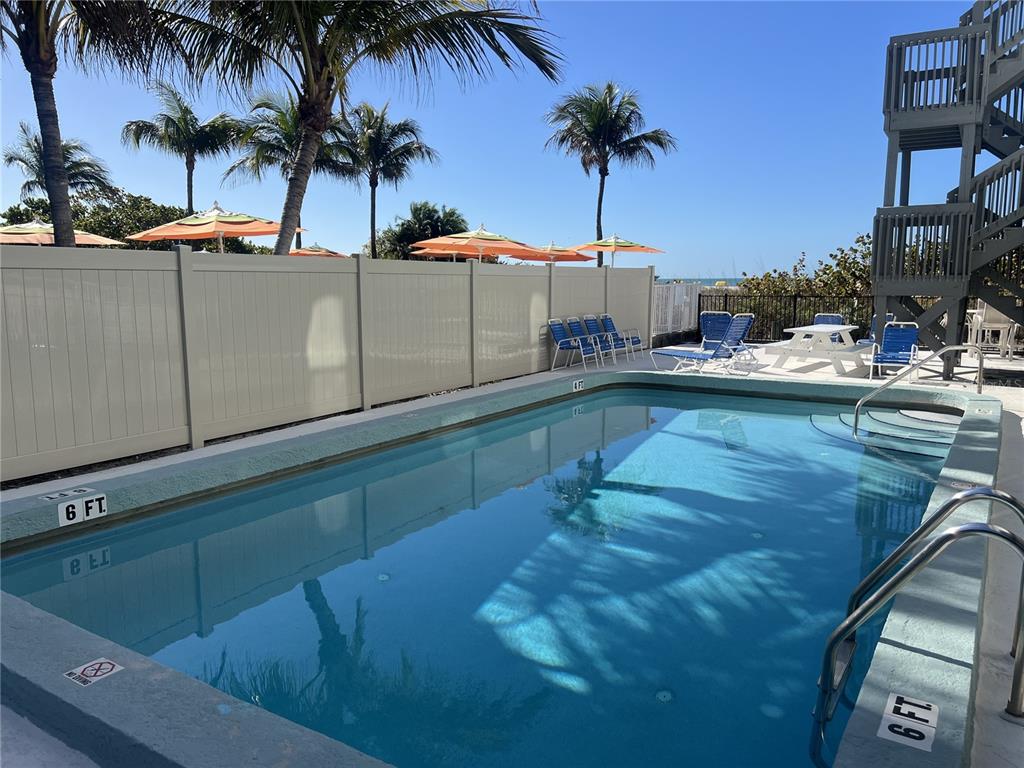 A rectangular swimming pool sits on a patio with lounge chairs and a privacy fence — 200 120TH AVENUE W UNIT 3A, TREASURE ISLAND, FL