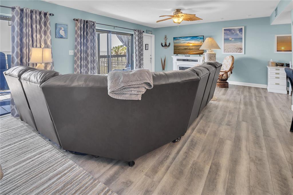 A living room features a large gray sectional sofa, light wood flooring, and blue walls — 200 120TH AVENUE W UNIT 3A, TREASURE ISLAND, FL