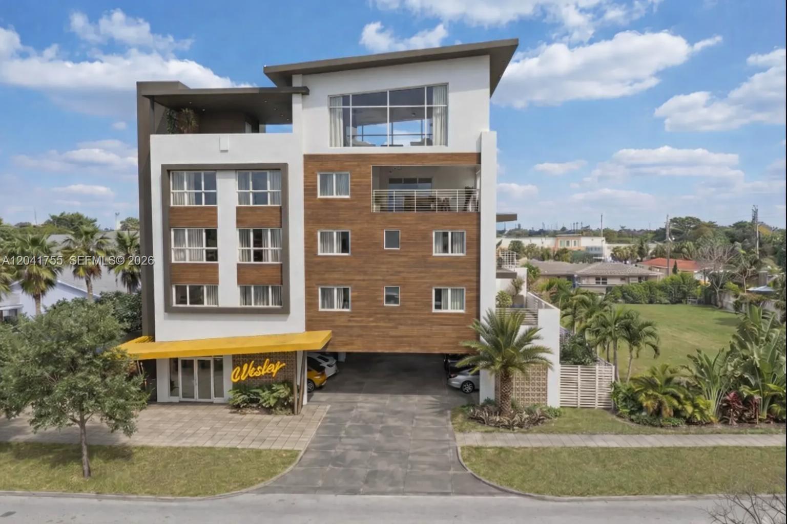 A modern multi-story apartment building features a wood-paneled facade, a ground-level parking area, and balconies — 2233 Fillmore St # 403, Hollywood FL 33020, HOLLYWOOD, FL