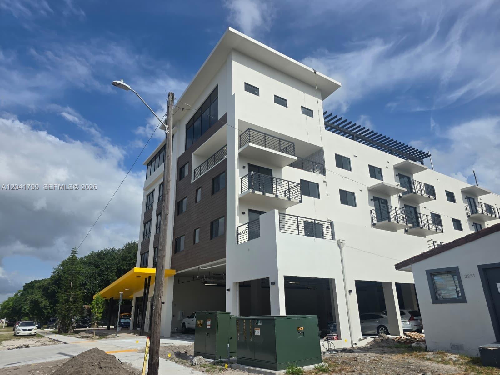 A modern multi-story apartment building with white stucco, wood-tone accents, and ground-level covered parking — 2233 Fillmore St # 403, Hollywood FL 33020, HOLLYWOOD, FL