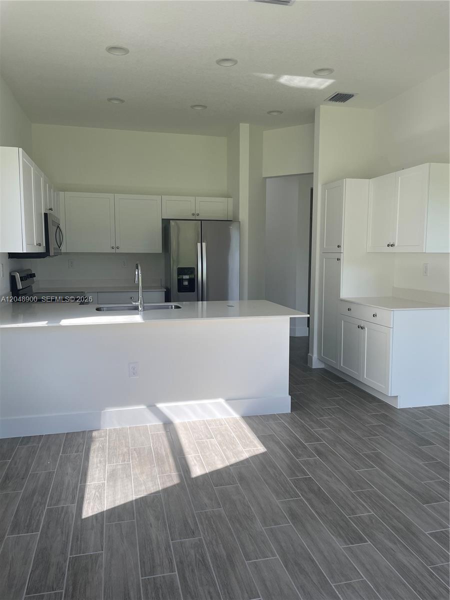 A modern kitchen features white cabinets, stainless steel appliances, and gray wood-look tile flooring — 5496 Agostino Way, Ave Maria FL 34142, AVE MARIA, FL
