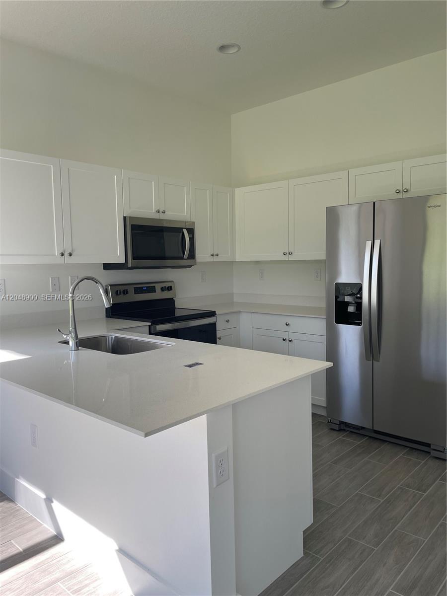 A modern kitchen features white cabinets, stainless steel appliances, and a quartz-topped island — 5496 Agostino Way, Ave Maria FL 34142, AVE MARIA, FL