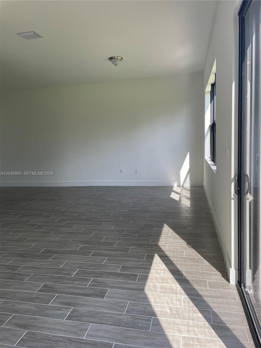An empty room features white walls, gray wood-look tile flooring, and a sliding glass door — 5496 Agostino Way, Ave Maria FL 34142, AVE MARIA, FL
