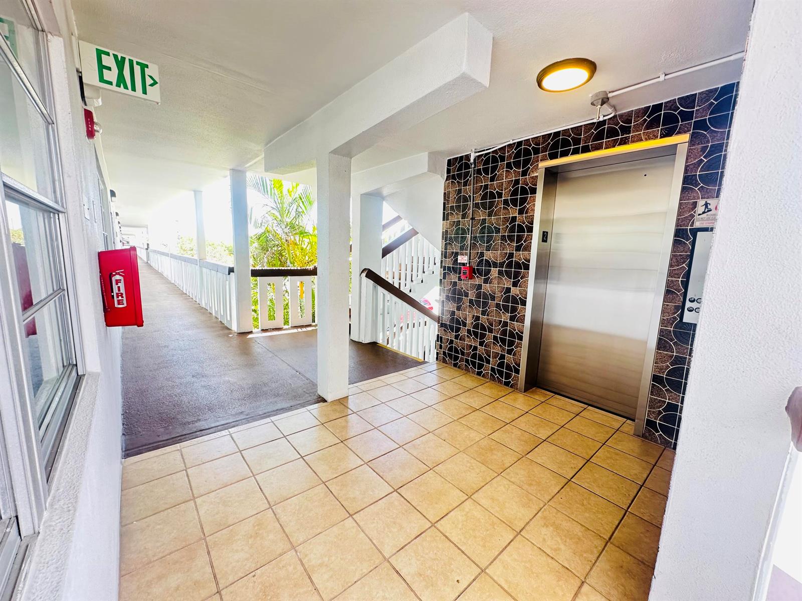 An outdoor apartment hallway features a tiled floor, an elevator, and a fire extinguisher box — 2060 Harwood E # 2060, Deerfield Beach FL 33442, DEERFIELD BEACH, FL