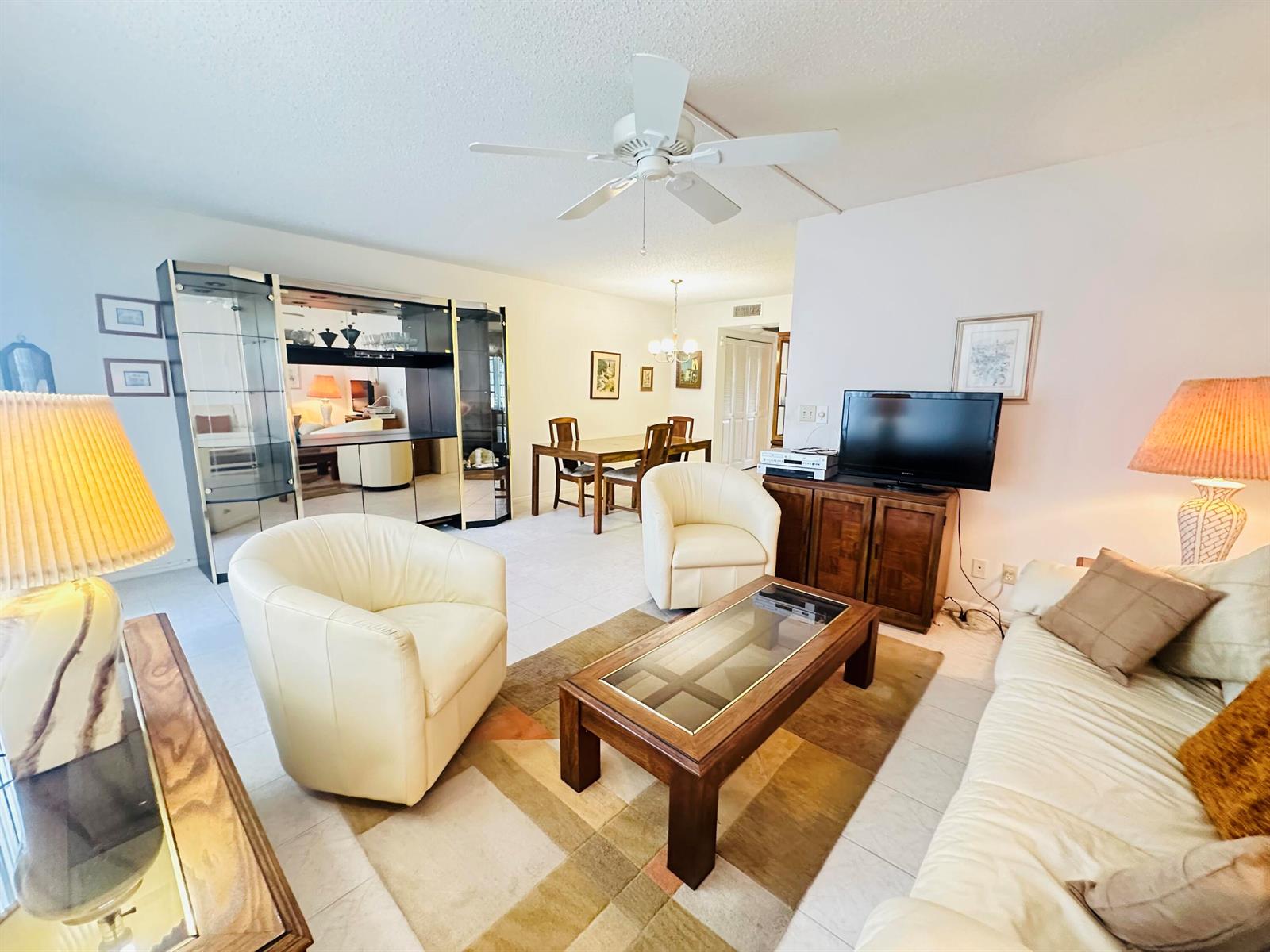 A living room with white armchairs, a wooden coffee table, and a dining area beyond — 2060 Harwood E # 2060, Deerfield Beach FL 33442, DEERFIELD BEACH, FL