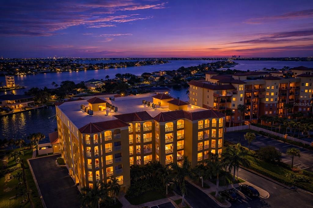 An aerial view of a multi-story yellow apartment building at sunset near a waterfront — 5353 GULF BOULEVARD UNIT A404, ST PETE BEACH, FL
