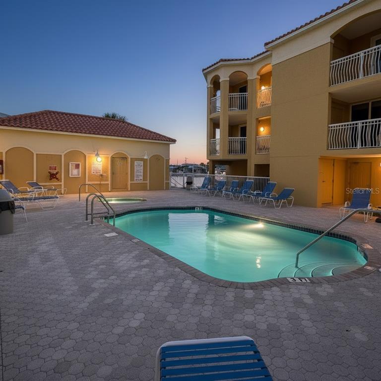 A swimming pool sits on a paved patio beside a multi-story building at dusk — 5353 GULF BOULEVARD UNIT A404, ST PETE BEACH, FL