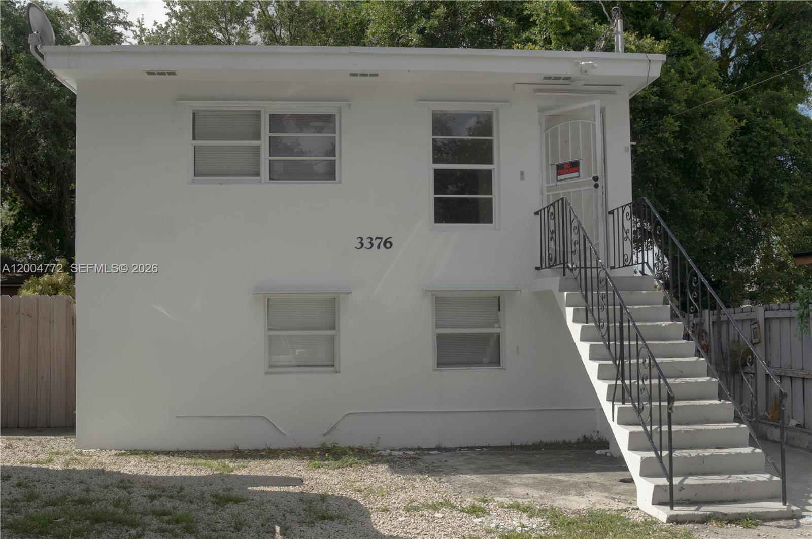 A two-story white stucco building features an exterior staircase leading to an upper-level entrance — 3376 NW 49th St, Miami FL 33142, MIAMI, FL