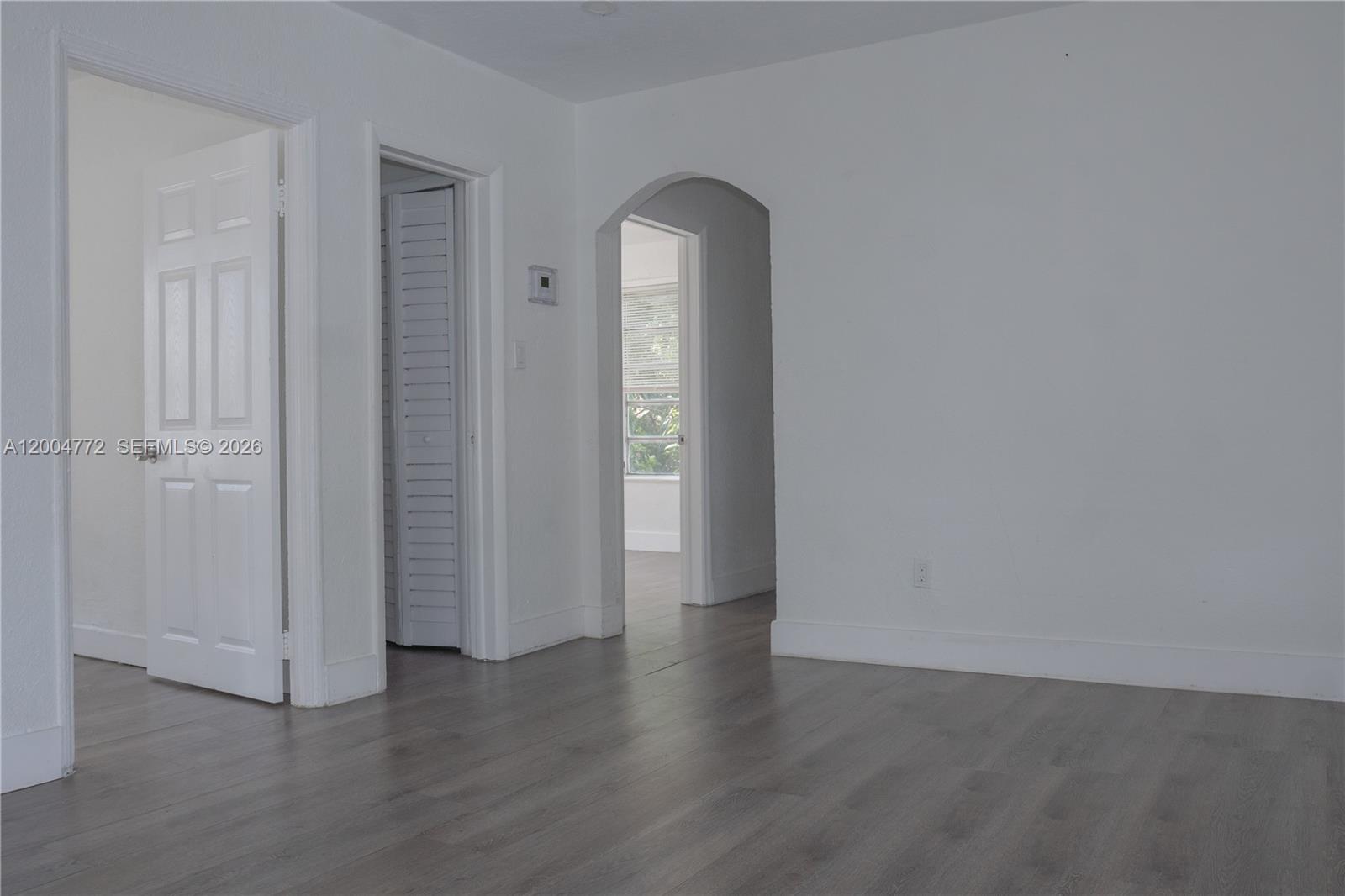An interior room features white walls, gray wood-look flooring, and an arched doorway — 3376 NW 49th St, Miami FL 33142, MIAMI, FL