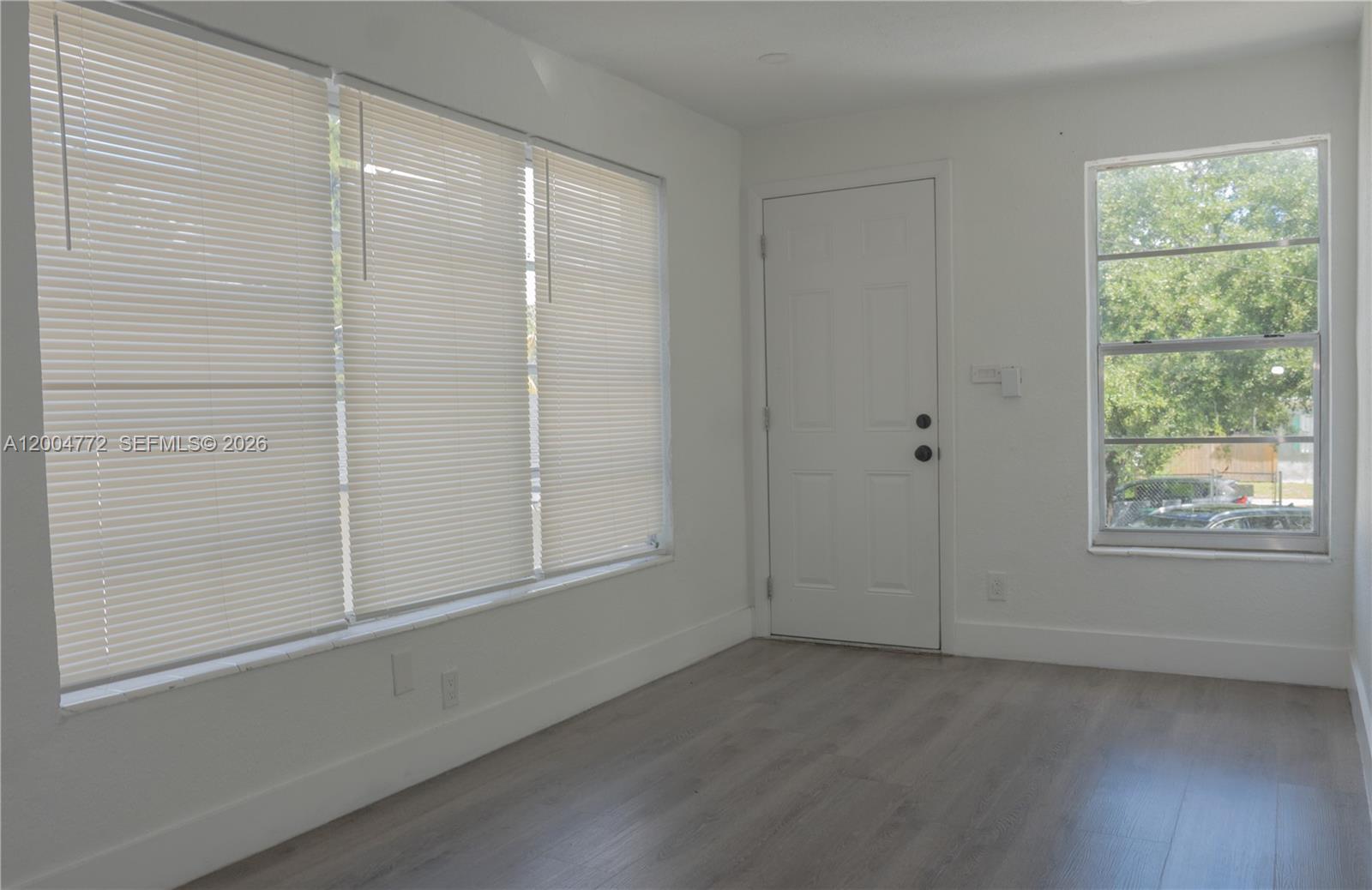 A room with white walls, light wood-look flooring, a white door, and large windows — 3376 NW 49th St, Miami FL 33142, MIAMI, FL