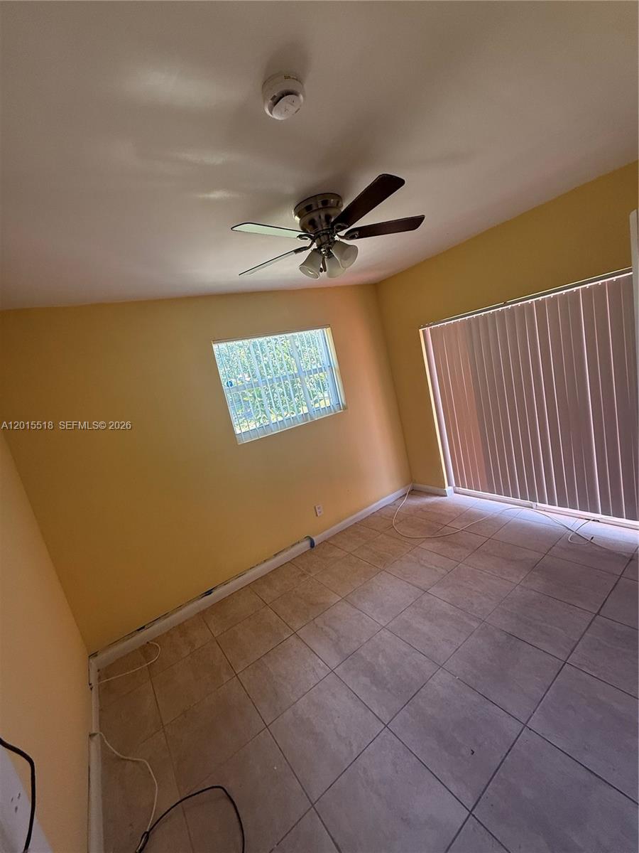 An empty room features yellow walls, tile flooring, a ceiling fan, and vertical blinds — NORTH MIAMI BEACH, FL