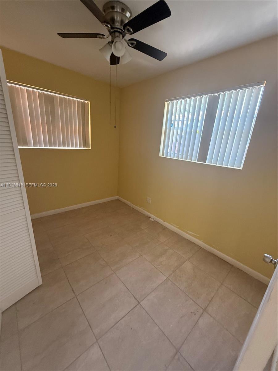 A small room features yellow walls, tile flooring, a ceiling fan, and two windows — NORTH MIAMI BEACH, FL