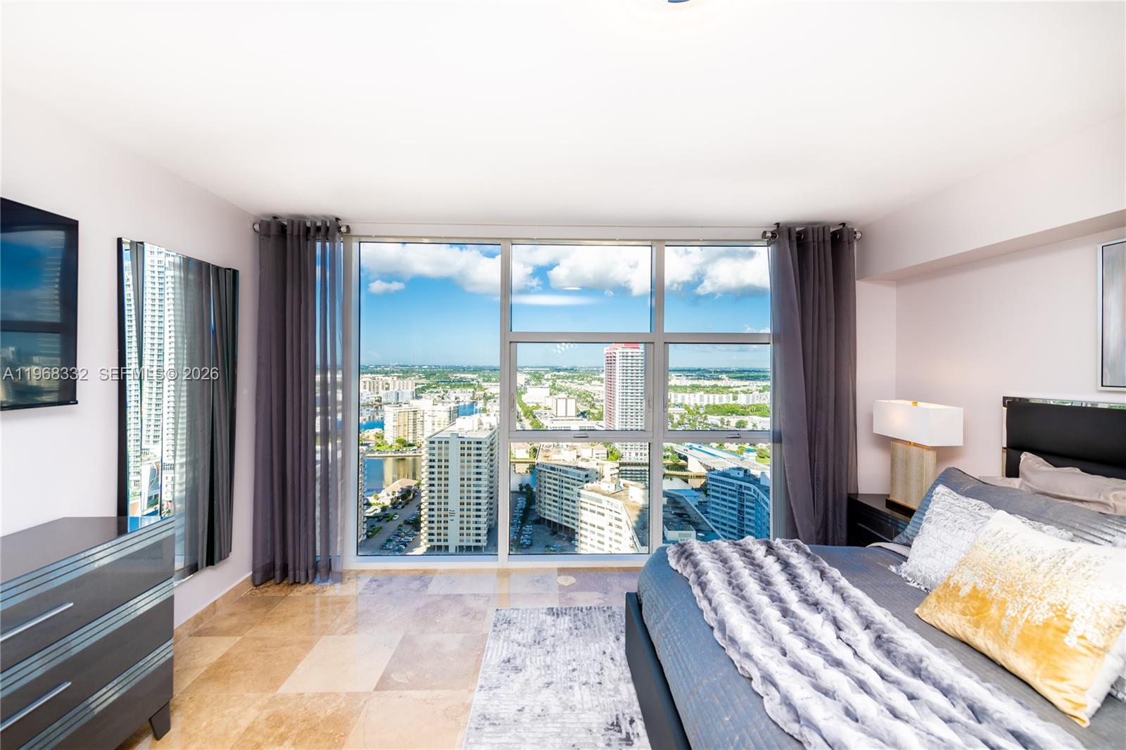 A bedroom with tile floors, a large bed, and floor-to-ceiling windows overlooking a city skyline — 1830 S Ocean Dr # 2907, Hallandale Beach FL 33009, HALLANDALE BEACH, FL