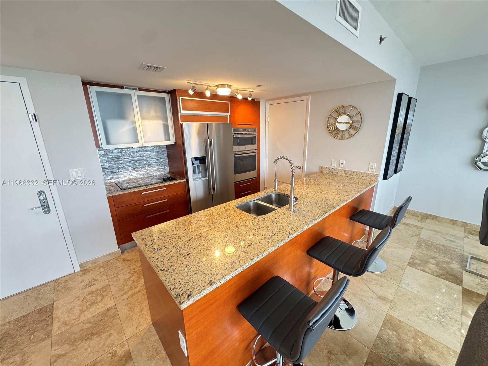 A kitchen features wood cabinets, granite countertops, a stainless steel refrigerator, and three bar stools — 1830 S Ocean Dr # 2907, Hallandale Beach FL 33009, HALLANDALE BEACH, FL