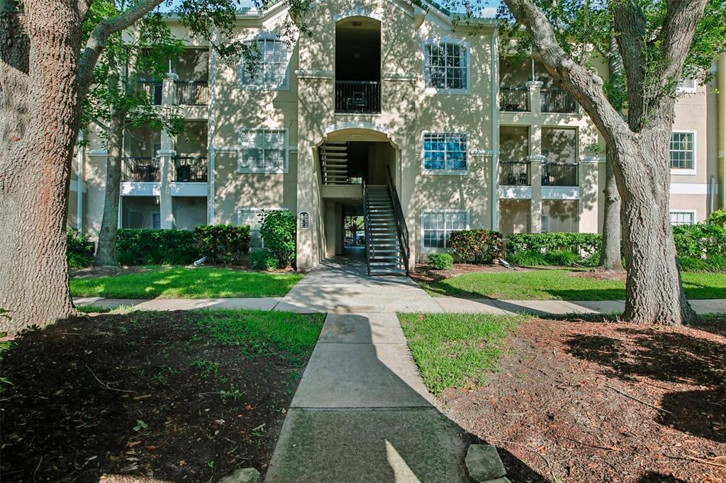 A sidewalk leads to the entrance and exterior staircase of a multi-story apartment building — 5174 NORTHRIDGE ROAD UNIT 104, SARASOTA, FL