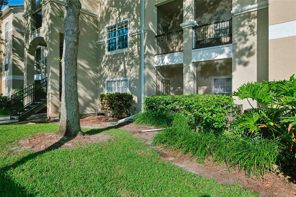 A multi-story apartment building exterior features a screened-in patio, green landscaping, and a large tree — 5174 NORTHRIDGE ROAD UNIT 104, SARASOTA, FL