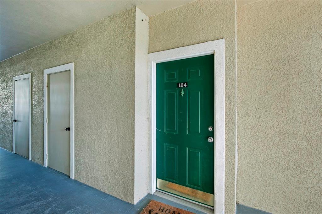 A green front door labeled 104 sits on a textured beige exterior wall — 5174 NORTHRIDGE ROAD UNIT 104, SARASOTA, FL