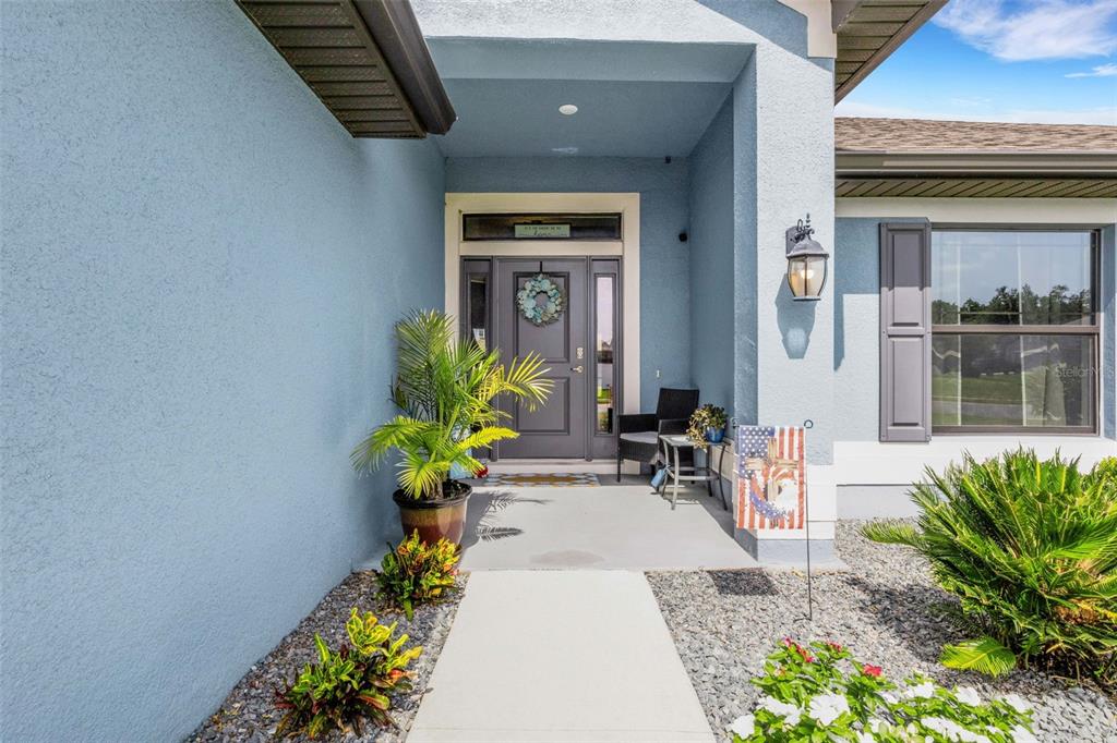 A blue house exterior features a covered entryway with a gray front door and landscaping — 220 HERITAGE PARK LANE, MULBERRY, FL