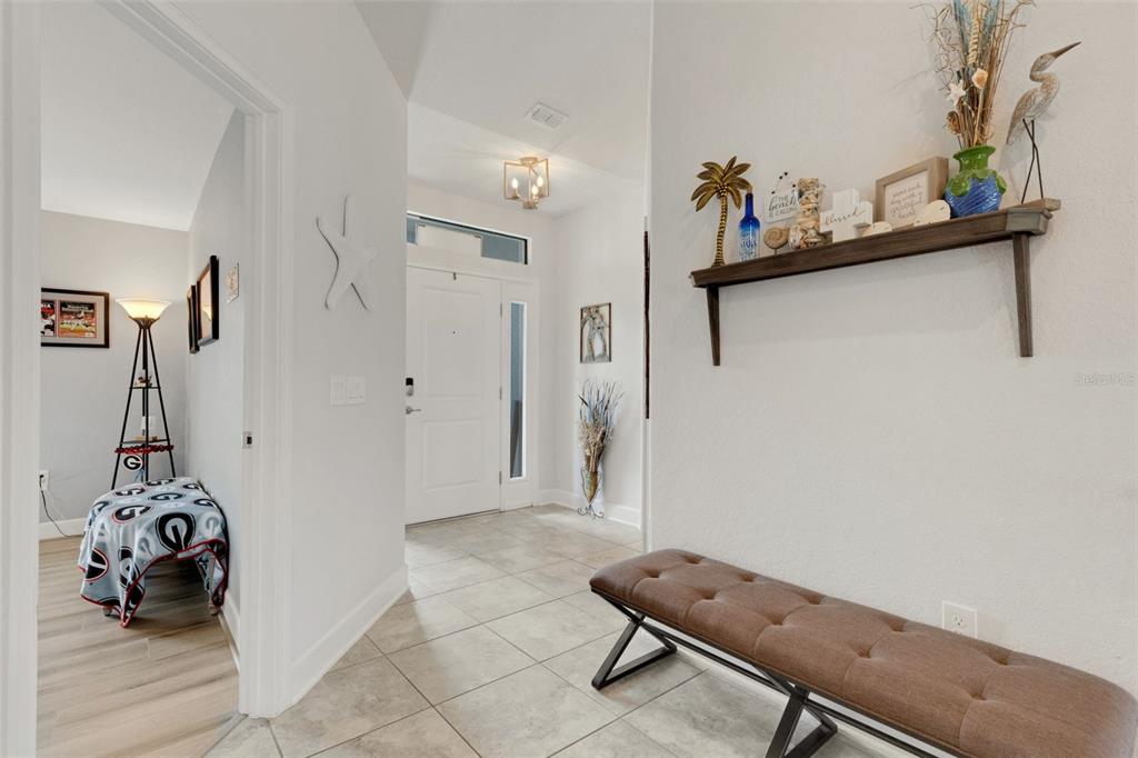 A bright entryway features tiled floors, a brown tufted bench, and a wall-mounted display shelf — 220 HERITAGE PARK LANE, MULBERRY, FL