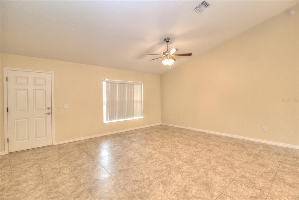 An empty room with beige walls, tile flooring, a ceiling fan, and a white door — 13 HEMLOCK TRACE COURT, OCALA, FL