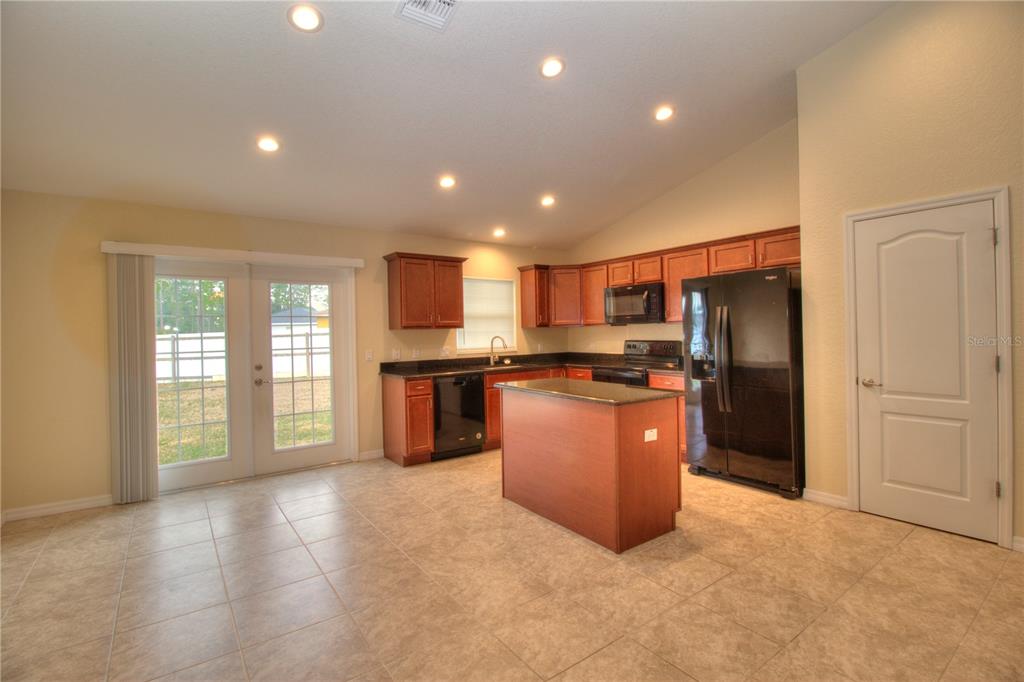 A kitchen features wood cabinets, black appliances, a center island, and tile flooring — 13 HEMLOCK TRACE COURT, OCALA, FL