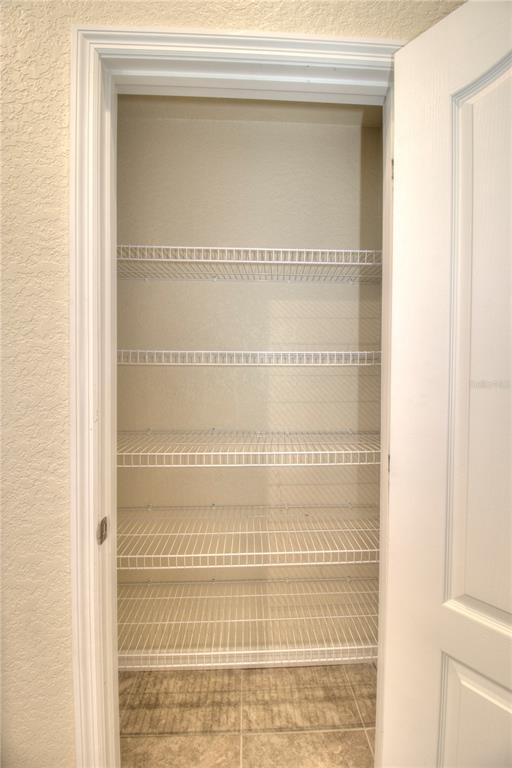A pantry with white wire shelving and tile flooring viewed through an open door — 13 HEMLOCK TRACE COURT, OCALA, FL