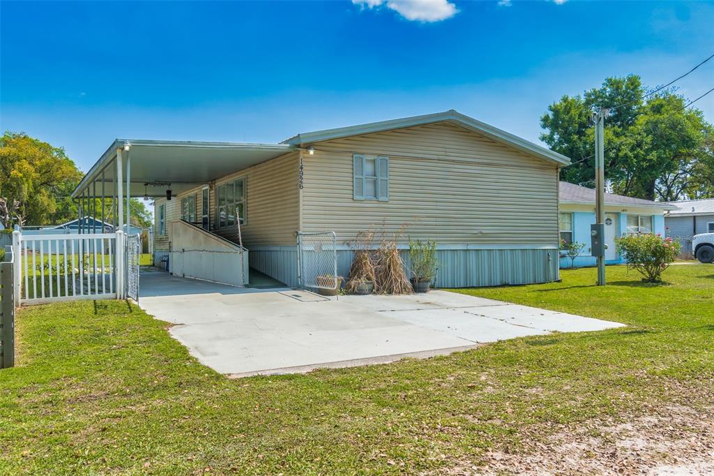 A single-story manufactured home with a carport, a wheelchair ramp, and a concrete driveway — 14926 DOUGLAS STREET, DADE CITY, FL