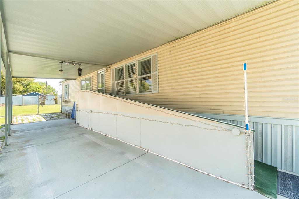 A concrete carport features a long, white wheelchair ramp leading to the side of a home — 14926 DOUGLAS STREET, DADE CITY, FL