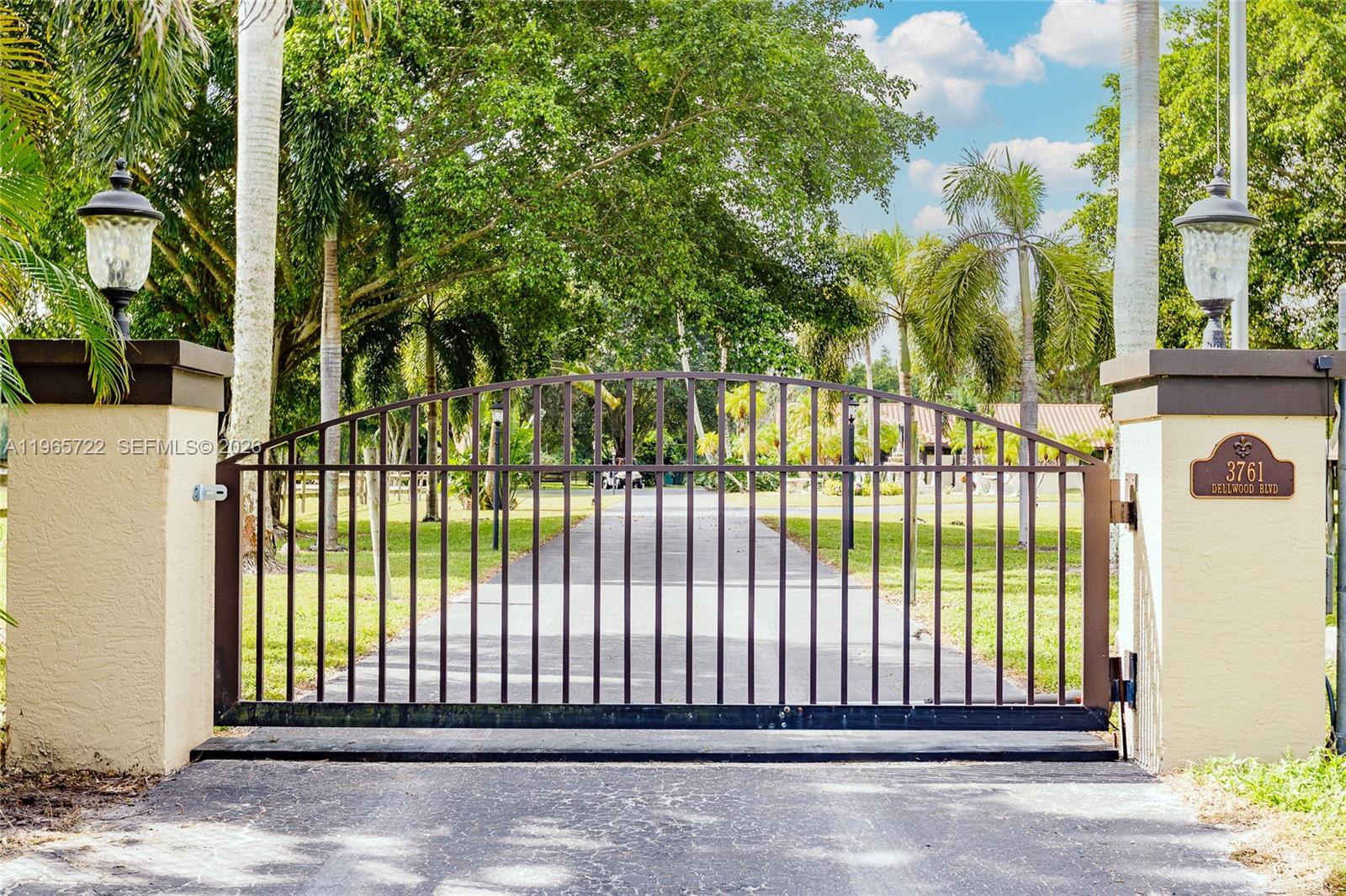 A metal driveway gate stands between two stucco pillars topped with outdoor lanterns — 3761 Dellwood Blvd., Loxahatchee FL 33470, LOXAHATCHEE, FL