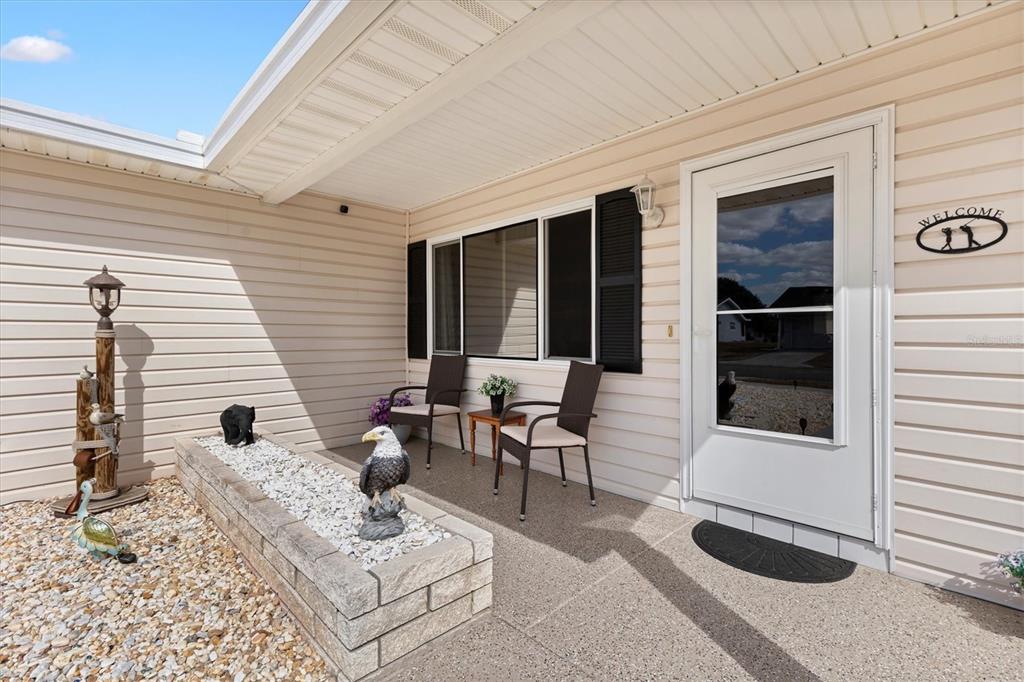 A covered front porch features a stone planter, two chairs, and a white entry door — 17587 SE 96TH COURT, SUMMERFIELD, FL
