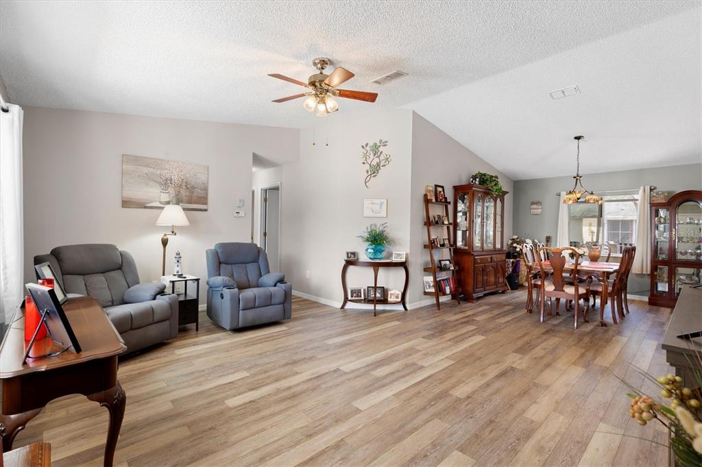 A living and dining area with wood-look flooring, a ceiling fan, and vaulted ceilings — 17587 SE 96TH COURT, SUMMERFIELD, FL