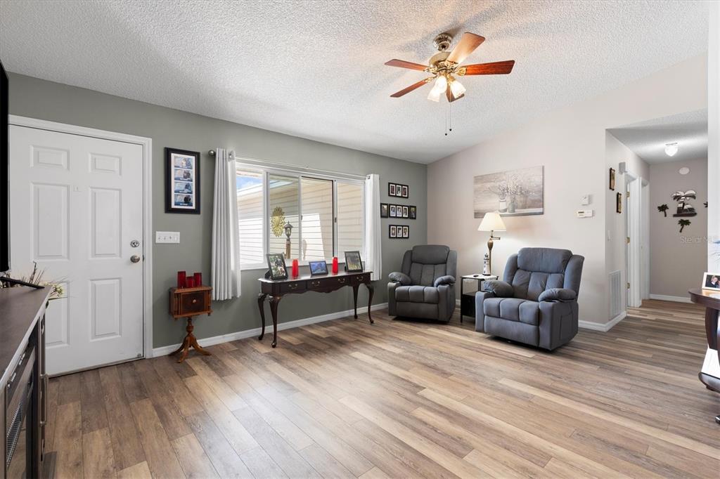 A living room features wood-look flooring, two gray recliners, a console table, and a ceiling fan — 17587 SE 96TH COURT, SUMMERFIELD, FL